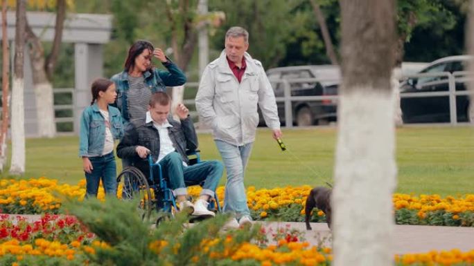 幸福一家人带着儿子坐在轮椅上走在路上，狗在附近奔跑。少年与父母，姐姐和狗散步的机会有限。