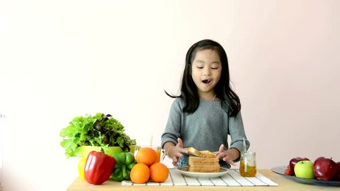 可爱的女孩在餐桌上撒播和吃果酱吐司