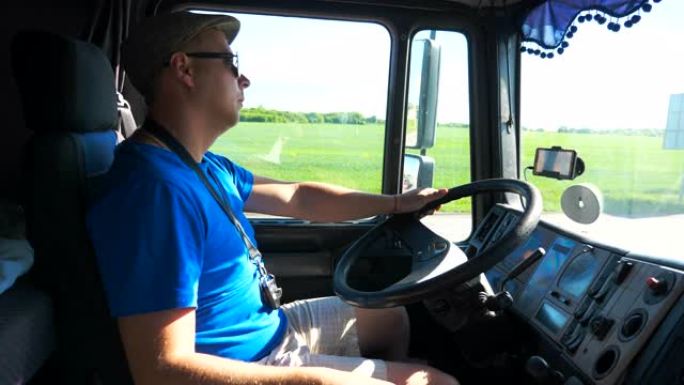 戴着墨镜的驾驶员的个人资料坐在卡车的方向盘后面，在阳光明媚的日子里骑在乡间小路上。男子控制他的卡车专