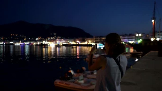 一名年轻女子通过电话拍摄克里特岛的夜海岸
