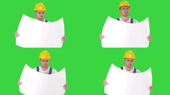 头戴头盔的体贴建设者看着蓝图，走在绿屏上，色键