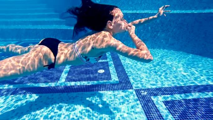 迷人的青少年在豪华游泳池水下游泳，用手关闭鼻子，慢动作