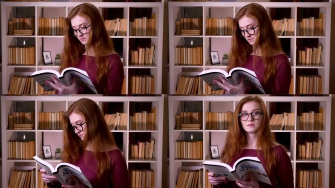 戴着眼镜的年轻红发迷人白人女学生的特写肖像看着相机，在大学图书馆微笑着看书