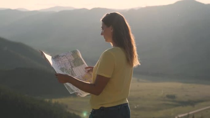 女游客站在悬崖边上，手里拿着地图，寻找旅行路线
