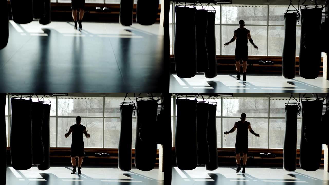 在健身房里，专业拳击手用跳绳做运动，同时在沙袋周围热身