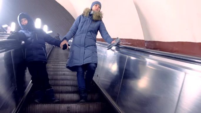 穿着冬装的妈妈和儿子正在地铁隧道中的自动扶梯上移动。