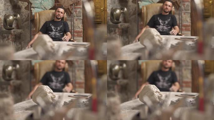 男性职业陶工坐在他的工作室里的前视图。创造陶瓷产品概念。背景时尚研讨会。选择性聚焦镜头