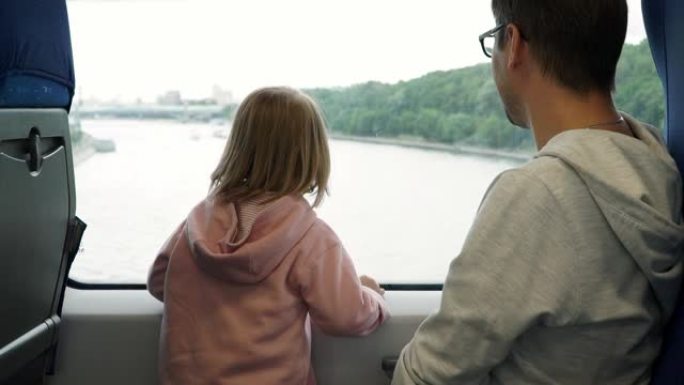 幸福的家庭，年轻的父亲和小女儿乘火车环游城市，看着窗外。男人和孩子在窗外挥舞风景，用手指在窗户上画心