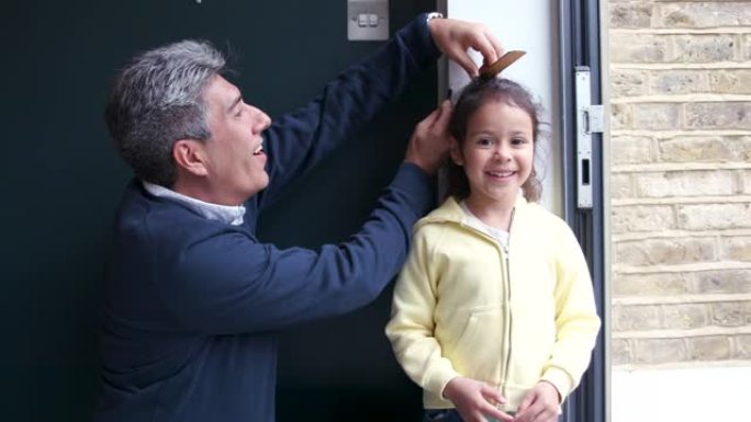 一位父亲在家里的墙上测量他的小女儿，看看她有多高