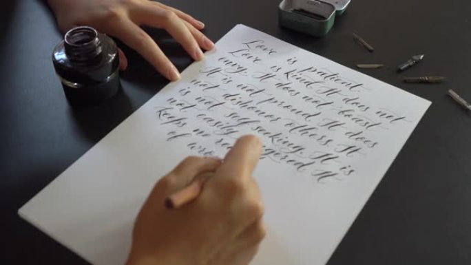 一个年轻女子使用刻字技术在纸上写字的特写镜头。她写了一个婚礼誓言爱是耐心的爱是善良的