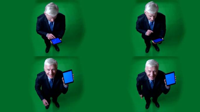 特写镜头使用平板电脑的老高加索商人的全高顶拍摄视图，并显示蓝屏到相机，背景隔离在绿色