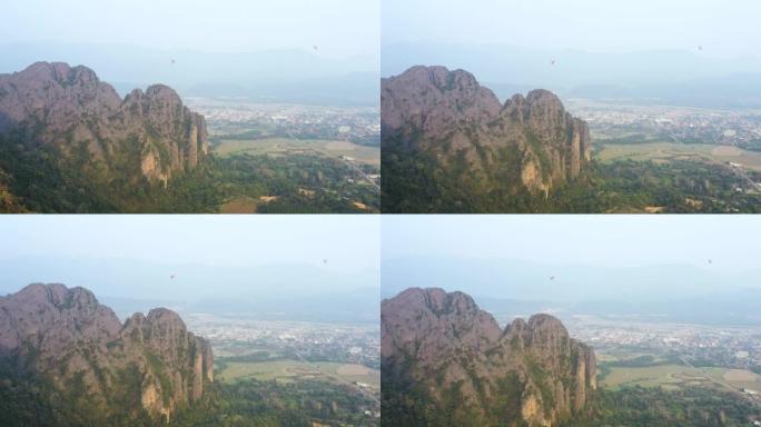 从上面看，前景中一座美丽的石灰岩山的惊人鸟瞰图，背景中一些热气球。老挝万维。
