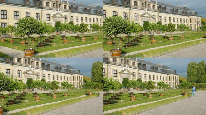 德国汉诺威。在美丽的中世纪宫殿附近种植了柑橘和橘子的树林。手持地图的年轻女游客进入框架。回去。慢动作