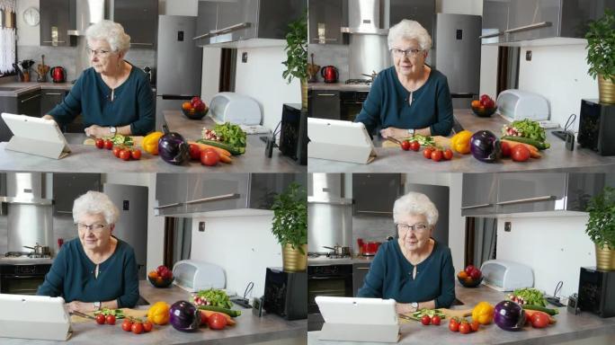 快乐的高级活跃女性在现代厨房在家做饭，在互联网电脑平板电脑上寻找食谱