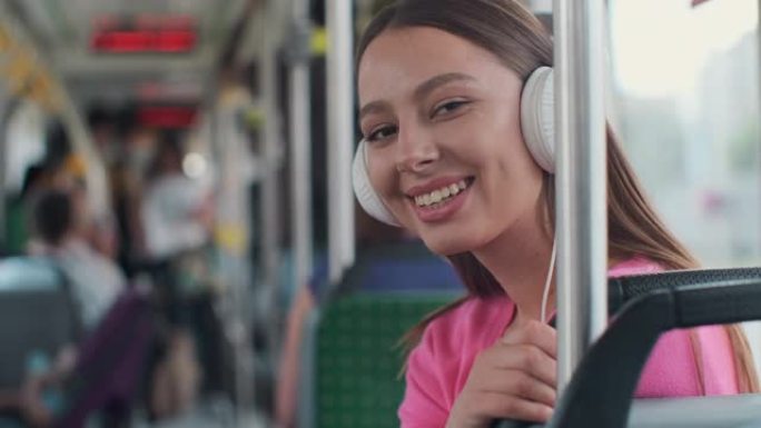 一位年轻女性乘客在公共交通工具上享受旅行的肖像，戴着耳机坐在现代电车上。