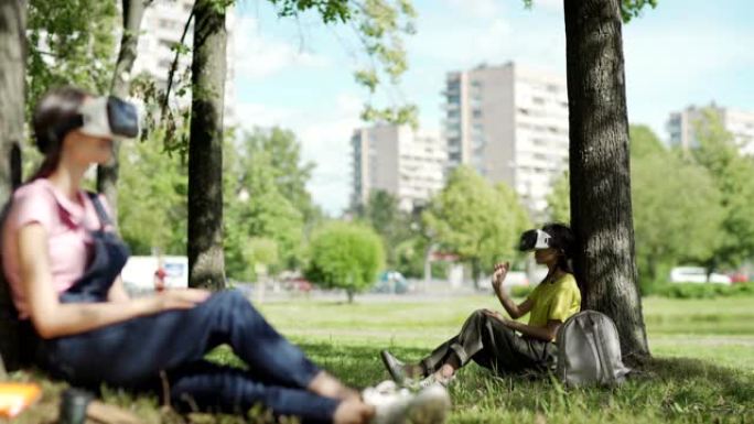 虚拟现实耳机中的亚洲女学生在公园的树下滑动可视化数据。散焦的女大学生戴着虚拟现实眼镜，在前景中放松音