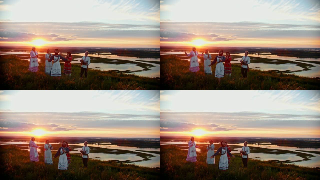 穿着俄罗斯传统服装的年轻人站在美丽的日落和唱歌的背景下。