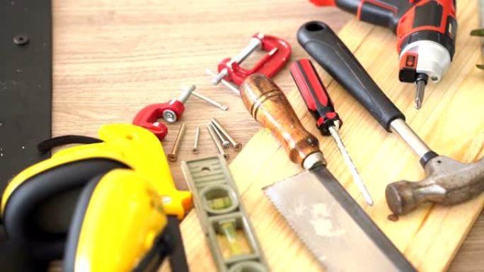 dolly shot的俯视图: 木制工匠的工作工具，例如锤子，防护手套，水平仪，无绳螺丝刀钻和刀