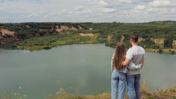 夫妇站在湖边的山崖上。恋爱中的情侣在美丽的自然观的背景下拥抱。空中。4K