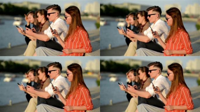 四个朋友在街上的智能手机中欢笑并观看社交媒体。每个人都有自己的电话。最好的朋友和学生在户外共度时光