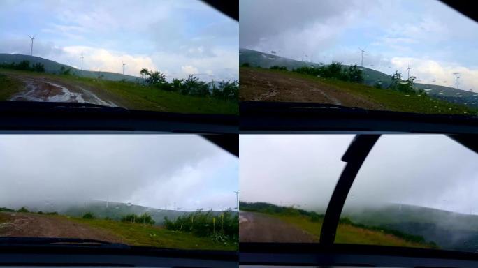 下午，在大雨中，POV在风力涡轮机公园的乡村道路上行驶