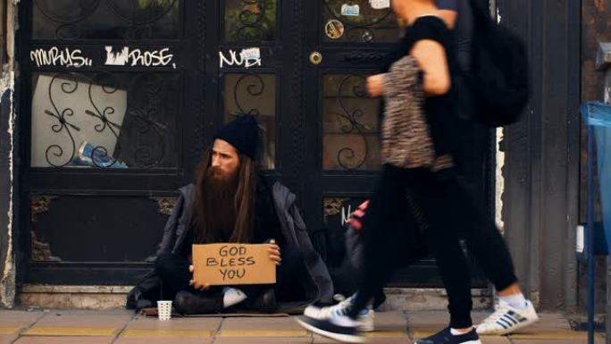 无家可归的人拿着 “上帝保佑你” 的纸板，在拥挤的街道上乞讨