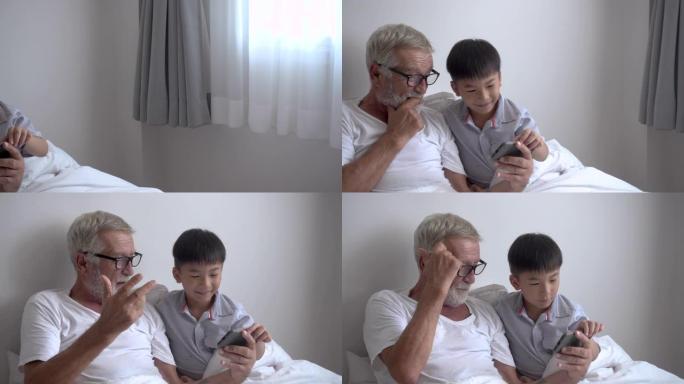 快乐的男孩孙子教年迈的老人祖父在疗养院的床上用智能手机玩游戏; 平移离开。