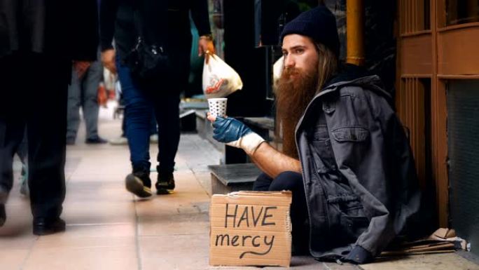 无家可归的人带着 “mercy” 纸板，在拥挤的街道上乞讨