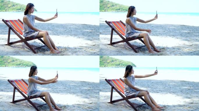 4k长镜头的年轻成年亚洲女性游客穿着夏装坐在沙滩椅日光浴床上放松或在热带岛屿海滩上享受日光浴暑假旅行