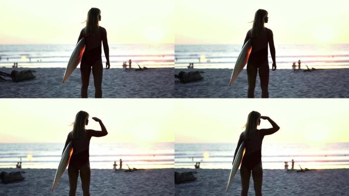 日落时海滩上冲浪板的冲浪女孩。健康积极的生活方式。