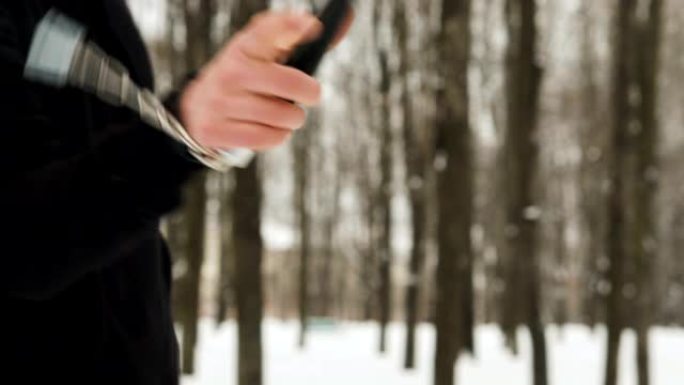 一个活跃的年轻人的手的特写镜头，一名武术战士，穿着黑色衣服，在冬天表演拳打双节棍的技巧，白雪覆盖的城