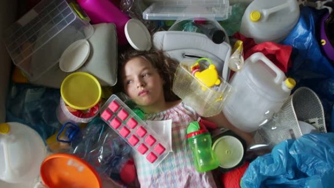 生态观念，塑料污染的威胁。女孩躺在一堆多色塑料里。垃圾落在她身上，她哭了
