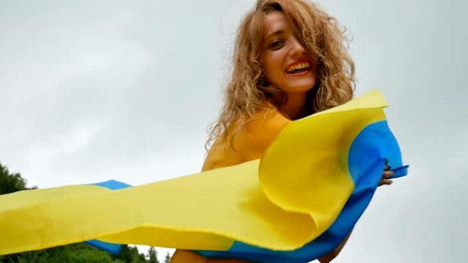 笑着快乐的年轻女孩与蓝色和黄色的乌克兰国旗在她的手在天空的背景