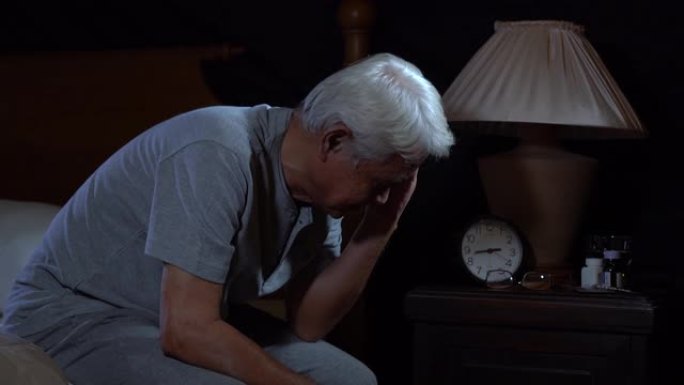 一个沮丧的老年人坐在床上无法失眠