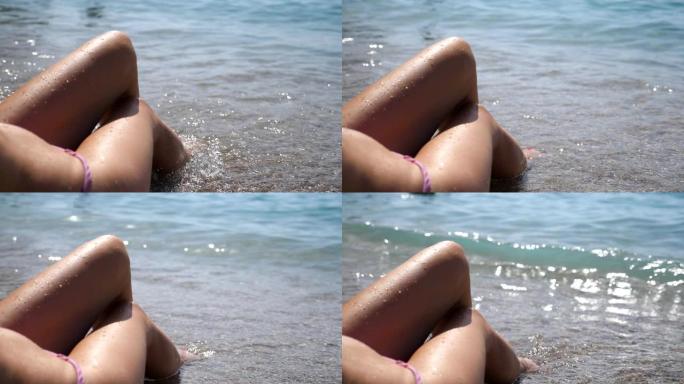 在阳光明媚的日子里，性感女孩晒得黝黑的脚躺在海滩上。无法辨认的女人在海边晒日光浴，在暑假放松。海浪洗