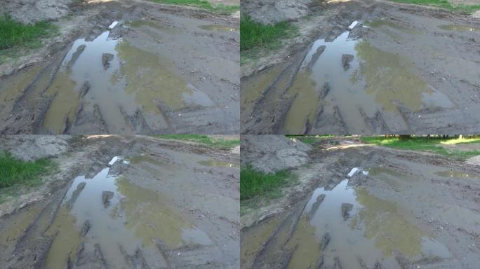 泥泞的土路上的泥泞和坑洼被重型机械摧毁，在洞中留下水，从上方看湿滑的地面，并直行移动