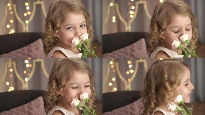 小女孩的特写镜头看着相机，微笑着闻到金色模糊花环背景下的粉红色玫瑰花朵。