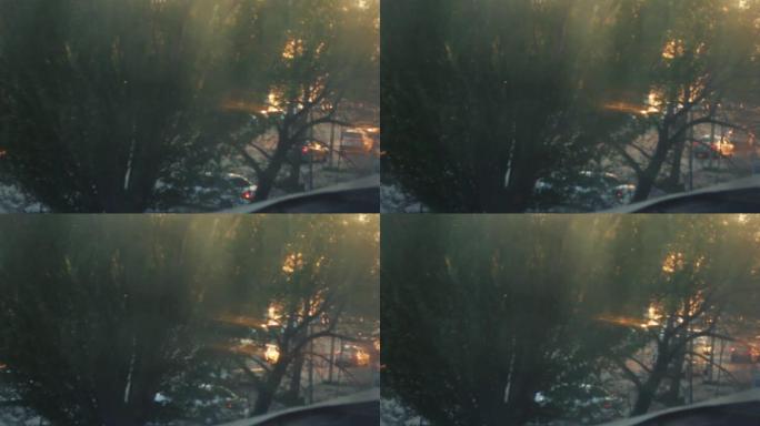散焦夜城，汽车交通灯。日落日模糊的画面。小雨在窗户上留下水滴。汽车在路上行驶并站立。