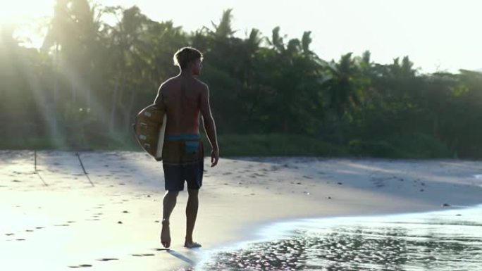 男性千禧一代在日出的灯光下带着冲浪板散步，玩得开心