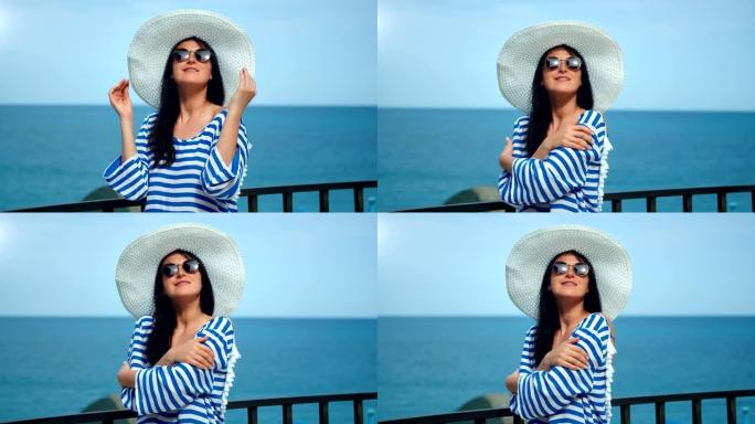 嬉戏的旅行时尚女人戴着白帽子和太阳镜在地平线海洋背景下摆姿势