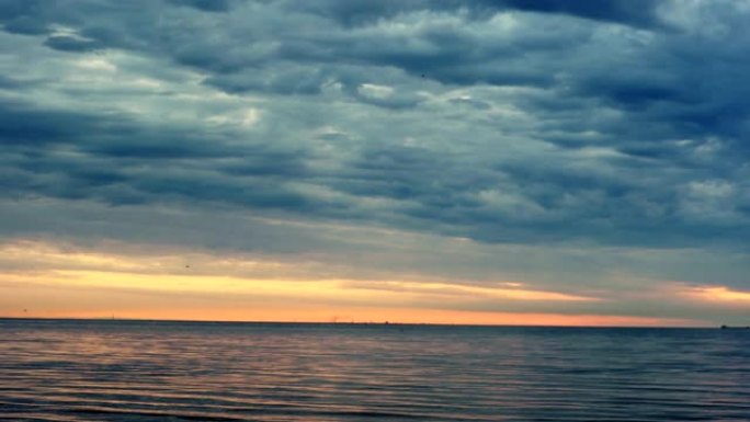 夕阳下的海景和夜空上的深蓝色云彩逐渐消失，鸟儿在水面上飞翔。美丽如画的日落风景