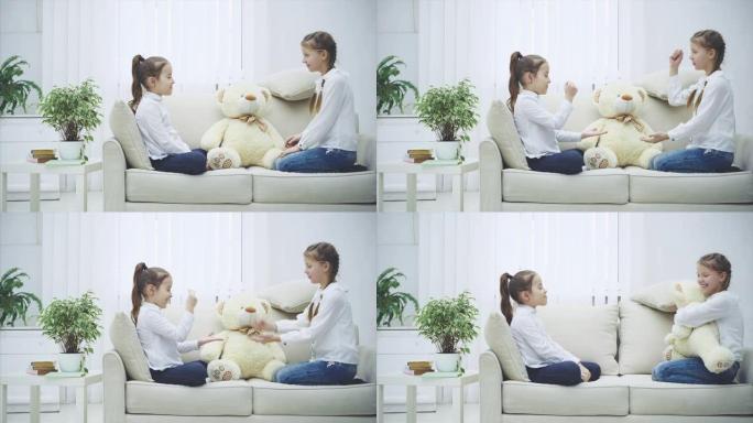 两个漂亮的女孩坐在沙发上，玩石头剪刀布，决定谁将与白色柔软的熊一起玩。