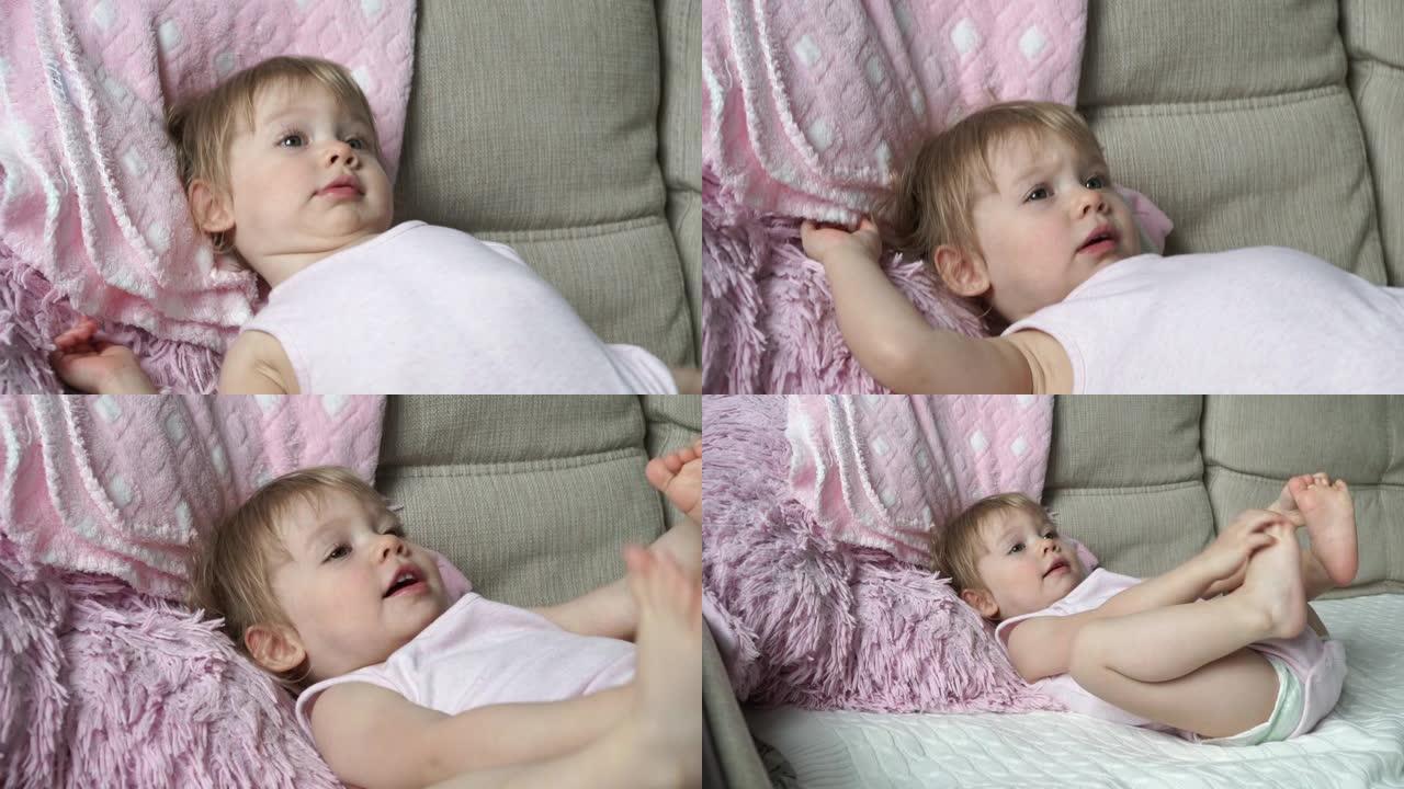 穿着粉红色衣服的2岁小女孩的肖像躺在床上，用脚玩耍，微笑着