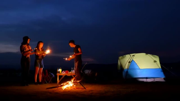 暑假期间，亚洲青少年在帐篷前与篝火一起玩耍，在湖边玩烟花。他们在假期，放松的时刻快乐并开心。青少年自