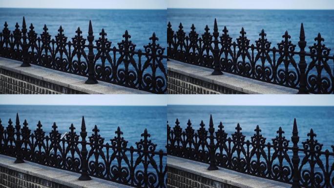 水的背景上的黑色金属栅栏。栏杆形式的装饰栅栏。摄像机沿着栅栏移动。特写