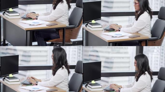 女商人坐在高层办公室的台式计算机上工作，倾斜镜头