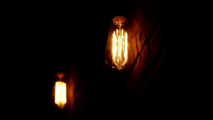 老式灯丝爱迪生灯泡。灯在黑暗中点亮。带有钨丝的白炽灯摆动。白炽灯的特写镜头。