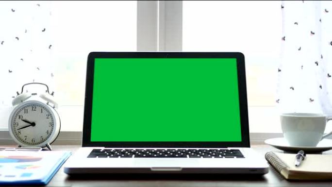 4K.笔记本电脑，带有绿色屏幕色度键，设置在靠近窗户的工作办公室桌子上，带有白色窗帘