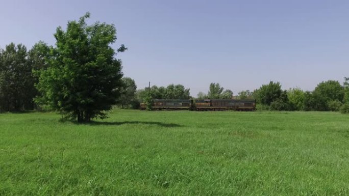 两辆机车列车在绿草成荫的铁路或铁轨上缓慢行驶，穿越大自然