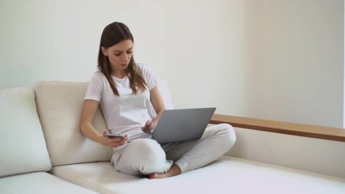 严肃的年轻女性博主在笔记本电脑和手机上工作，并通过互联网